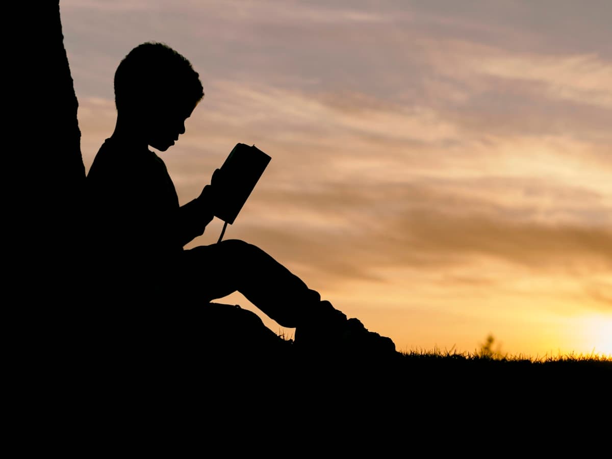 Barn som leser bok mot solnedgang